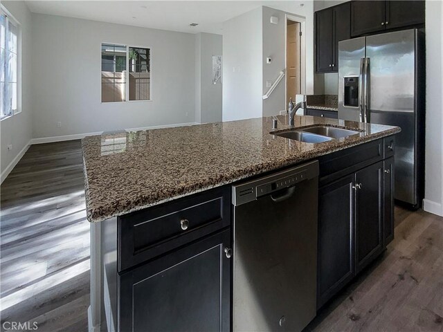 kitchen with sink, light stone counters, stainless steel fridge, black dishwasher, and a kitchen island with sink