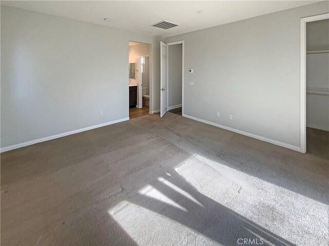 unfurnished bedroom featuring a walk in closet, connected bathroom, carpet floors, and a closet