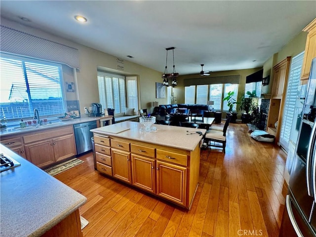 kitchen with sink, light hardwood / wood-style floors, a kitchen island, decorative light fixtures, and stainless steel dishwasher