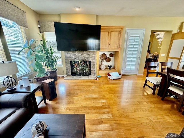 living room with a healthy amount of sunlight, a stone fireplace, and light hardwood / wood-style floors