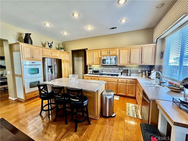 kitchen with light wood-type flooring, a kitchen island, sink, appliances with stainless steel finishes, and a kitchen bar