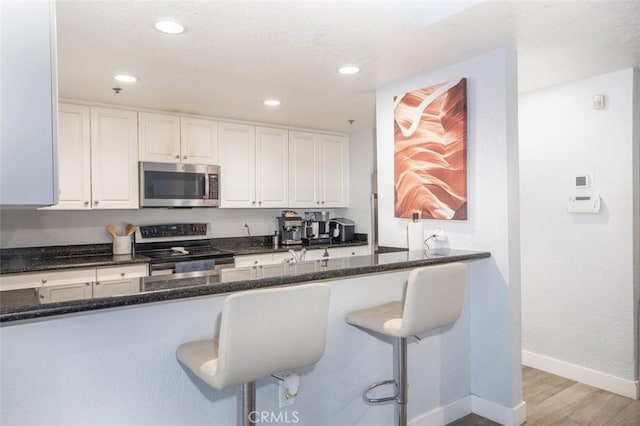 kitchen with dark stone countertops, white cabinetry, light hardwood / wood-style flooring, a kitchen breakfast bar, and stainless steel appliances