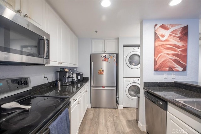 kitchen with light wood-type flooring, stacked washer and dryer, stainless steel appliances, white cabinets, and dark stone counters