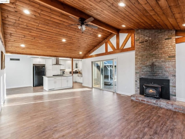 unfurnished living room featuring ceiling fan, beamed ceiling, hardwood / wood-style flooring, wood ceiling, and a wood stove