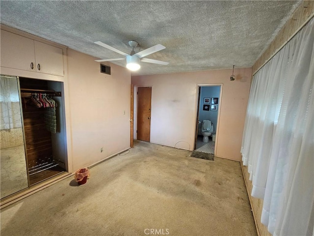 unfurnished bedroom with ceiling fan, a textured ceiling, ensuite bath, and a closet