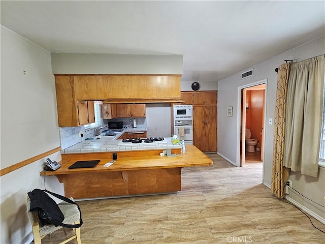 kitchen featuring sink, tile countertops, kitchen peninsula, white appliances, and decorative backsplash