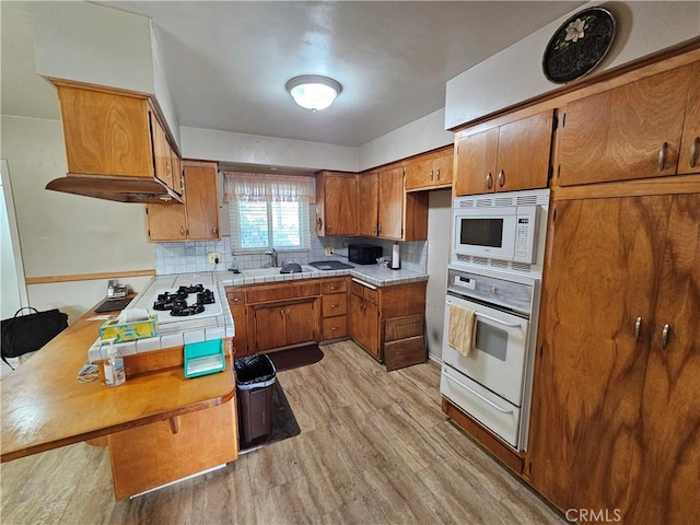 kitchen with tasteful backsplash, sink, white appliances, and light hardwood / wood-style flooring