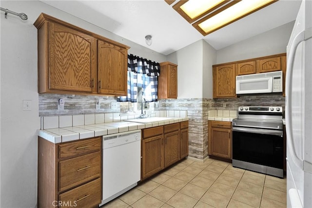 kitchen featuring lofted ceiling, tasteful backsplash, sink, white appliances, and light tile patterned floors