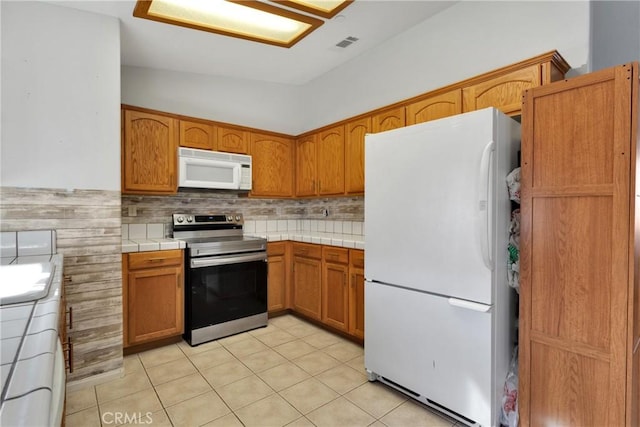 kitchen with light tile patterned flooring, tile counters, tasteful backsplash, and white appliances