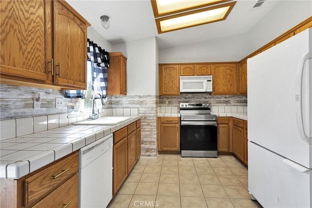 kitchen featuring vaulted ceiling, sink, white appliances, light tile patterned flooring, and tile counters