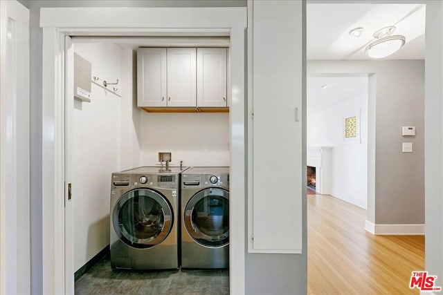 laundry room featuring washing machine and dryer, cabinets, light hardwood / wood-style floors, and a brick fireplace