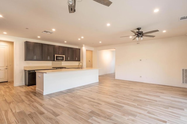 kitchen featuring an island with sink, sink, light wood-type flooring, ceiling fan, and dark brown cabinets