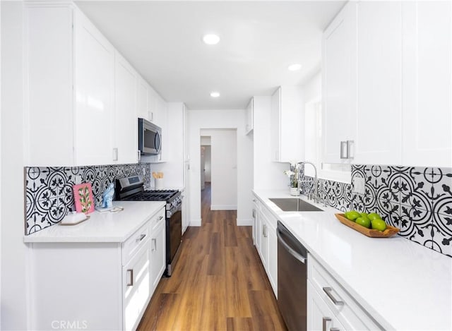 kitchen with appliances with stainless steel finishes, dark hardwood / wood-style floors, backsplash, white cabinets, and sink