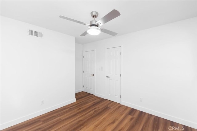 unfurnished bedroom featuring dark wood-type flooring, ceiling fan, and two closets