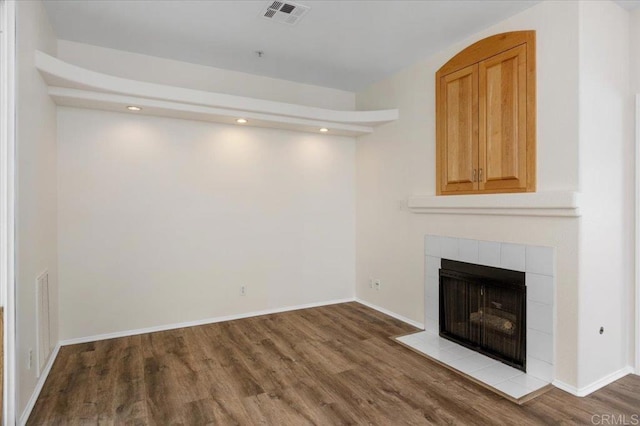 unfurnished living room with a tiled fireplace, wood finished floors, visible vents, and baseboards