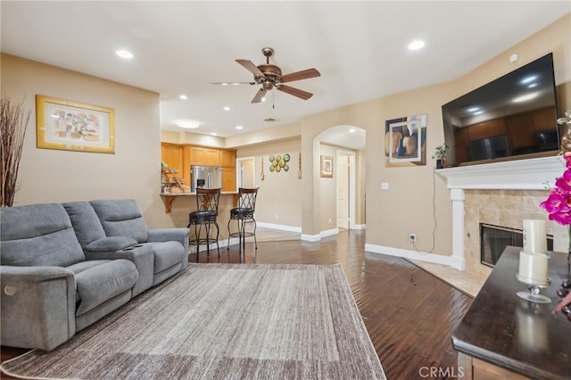 living room featuring a fireplace, ceiling fan, and dark wood-type flooring