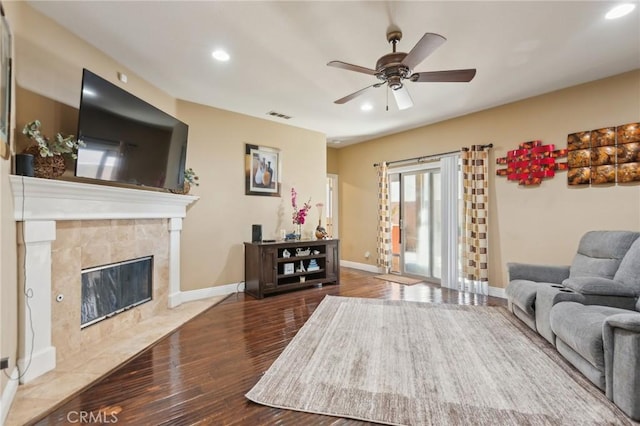 living room featuring hardwood / wood-style flooring, a tiled fireplace, and ceiling fan