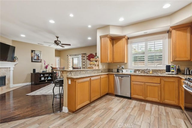 kitchen with a tile fireplace, appliances with stainless steel finishes, kitchen peninsula, sink, and light hardwood / wood-style flooring