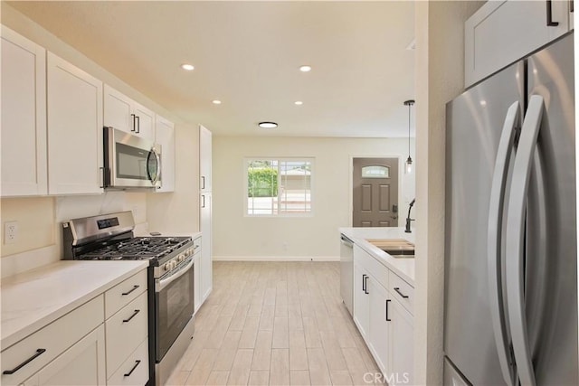 kitchen featuring sink, white cabinetry, stainless steel appliances, and hanging light fixtures