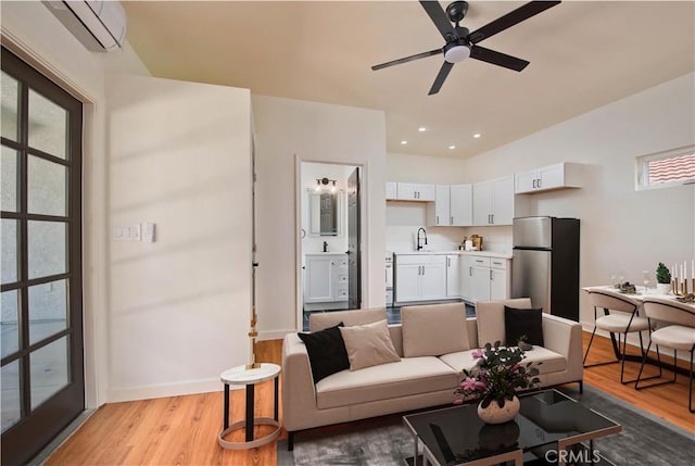 living room featuring ceiling fan, light wood-type flooring, an AC wall unit, and sink