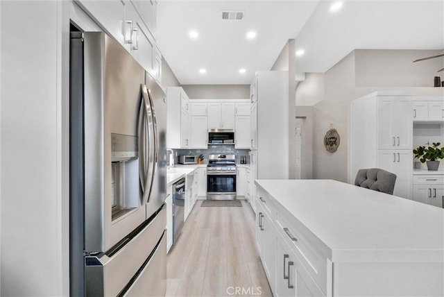 kitchen featuring white cabinets, decorative backsplash, appliances with stainless steel finishes, and light hardwood / wood-style flooring