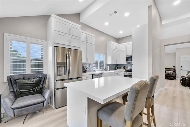 kitchen featuring tasteful backsplash, appliances with stainless steel finishes, a breakfast bar area, and white cabinetry