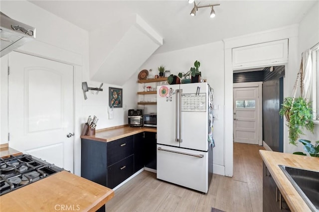 kitchen with white refrigerator, butcher block counters, sink, light wood-type flooring, and gas cooktop