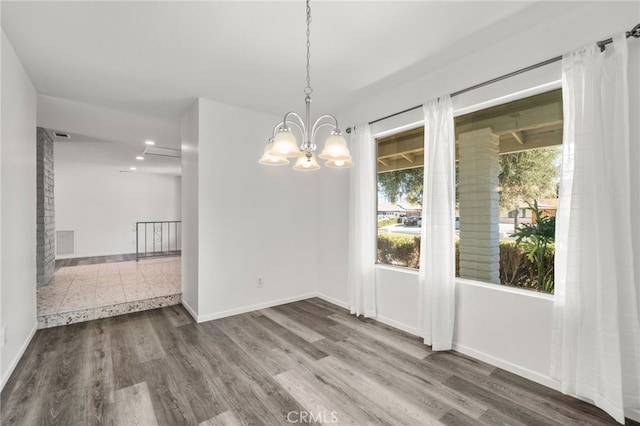 unfurnished dining area with a notable chandelier, visible vents, baseboards, and wood finished floors