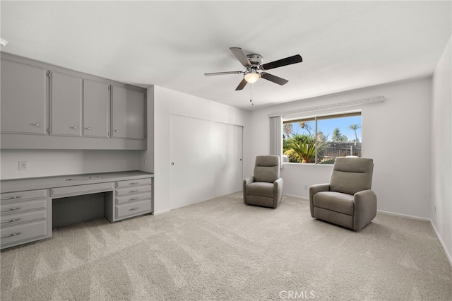 sitting room with built in desk, light colored carpet, and ceiling fan