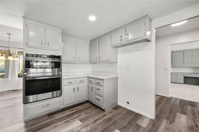 kitchen with dark wood-style floors, light countertops, an inviting chandelier, stainless steel double oven, and baseboards