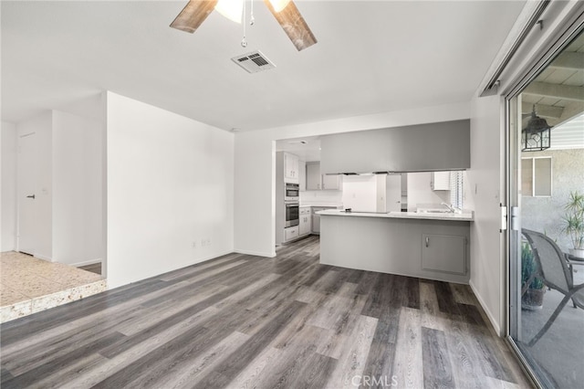 kitchen with visible vents, ceiling fan, dark wood-style flooring, a peninsula, and light countertops