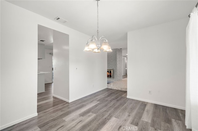 unfurnished dining area with baseboards, visible vents, wood finished floors, a fireplace, and a notable chandelier