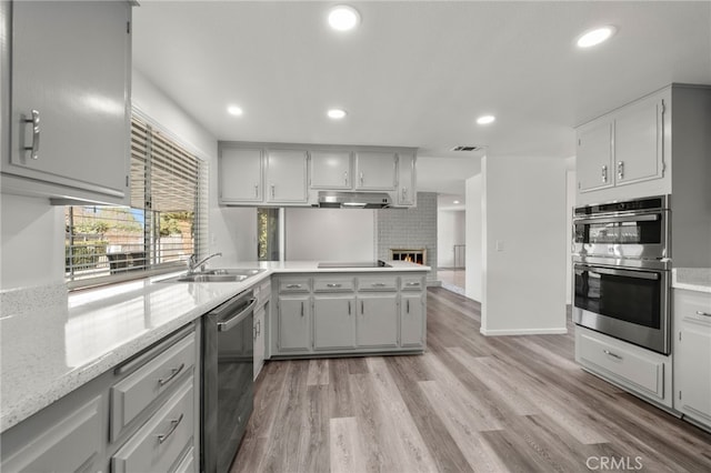 kitchen featuring appliances with stainless steel finishes, a peninsula, light wood-type flooring, a brick fireplace, and a sink