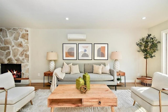 living room with an AC wall unit, a stone fireplace, and light hardwood / wood-style floors