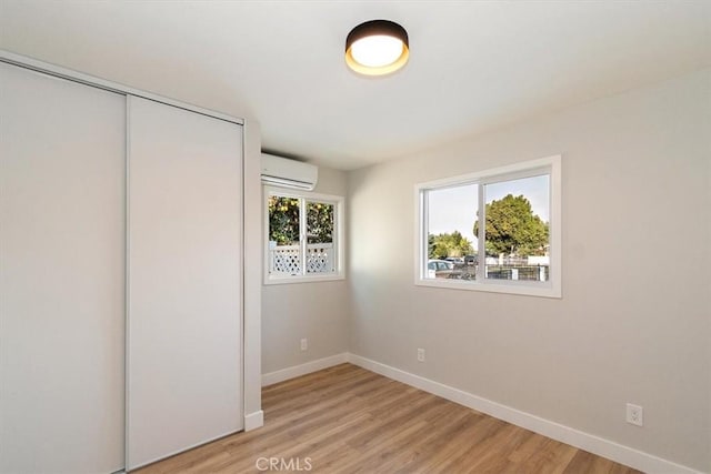 unfurnished bedroom featuring light hardwood / wood-style floors, an AC wall unit, and a closet