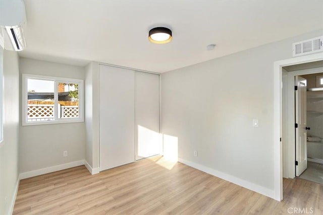 unfurnished bedroom featuring a closet, light hardwood / wood-style floors, and a wall mounted AC