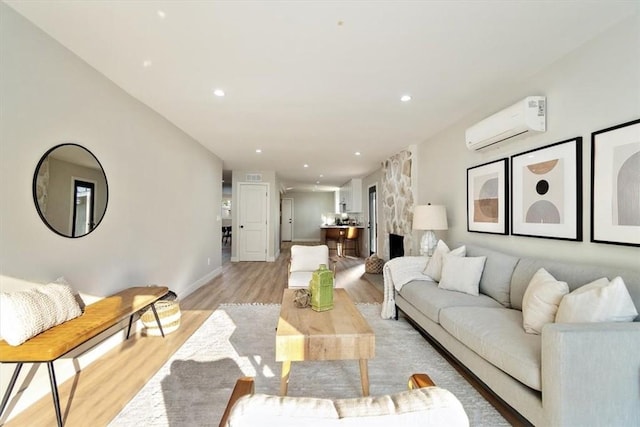 living room with a wall mounted air conditioner, light wood-type flooring, and a stone fireplace