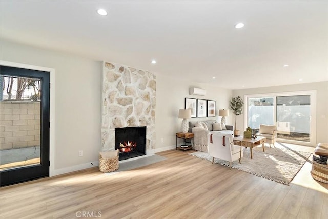 living room featuring a wall mounted AC, a fireplace, light hardwood / wood-style floors, and plenty of natural light