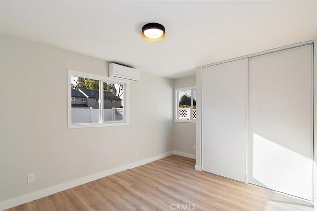 unfurnished bedroom featuring a wall mounted air conditioner, light wood-type flooring, multiple windows, and a closet