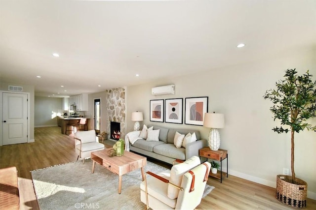 living room featuring a wall mounted AC, a stone fireplace, and light hardwood / wood-style floors