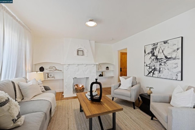 living room featuring light wood-type flooring, built in features, and a stone fireplace