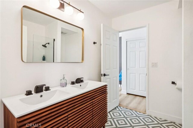 full bath with a sink, baseboards, double vanity, and walk in shower