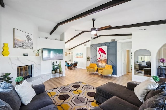 living room featuring vaulted ceiling with beams, ceiling fan with notable chandelier, a fireplace, and light wood-type flooring