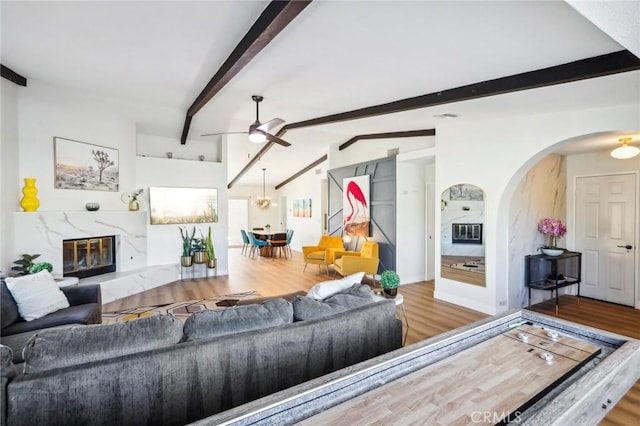 living room with ceiling fan, a high end fireplace, lofted ceiling with beams, and wood-type flooring