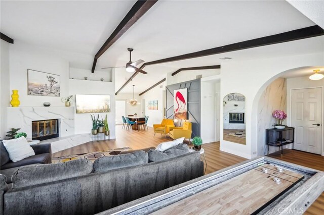 living room with arched walkways, vaulted ceiling with beams, wood finished floors, and a ceiling fan