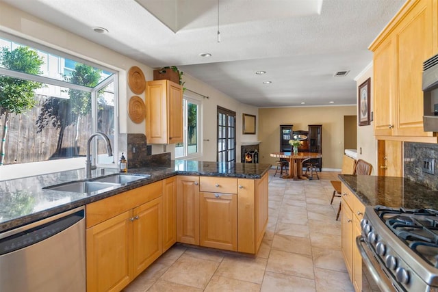 kitchen featuring backsplash, dark stone counters, sink, kitchen peninsula, and stainless steel appliances