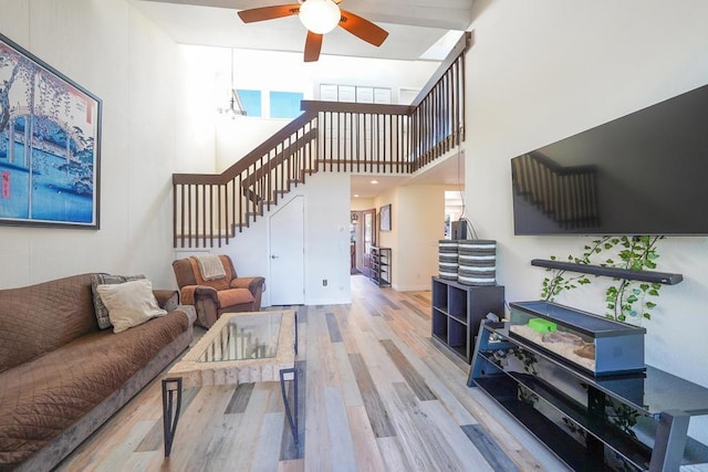 living room with ceiling fan, wood-type flooring, and a towering ceiling