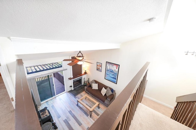 living room featuring ceiling fan, a textured ceiling, a tile fireplace, and lofted ceiling