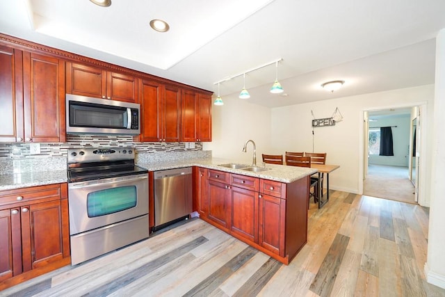 kitchen featuring kitchen peninsula, sink, appliances with stainless steel finishes, track lighting, and light stone counters