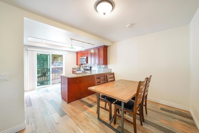 kitchen featuring light wood-type flooring, light stone countertops, kitchen peninsula, and sink